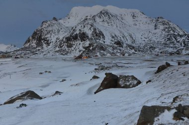 Sahilin eteklerindeki sahil kenarındaki çiftlik ve çiftliklere doğru bakan Utakleiv, plajı sınırlayan Molhiea-Malheia-Himmeltindan. Vestvagoya-Lofoten-Nordland Fylke-Norveç.