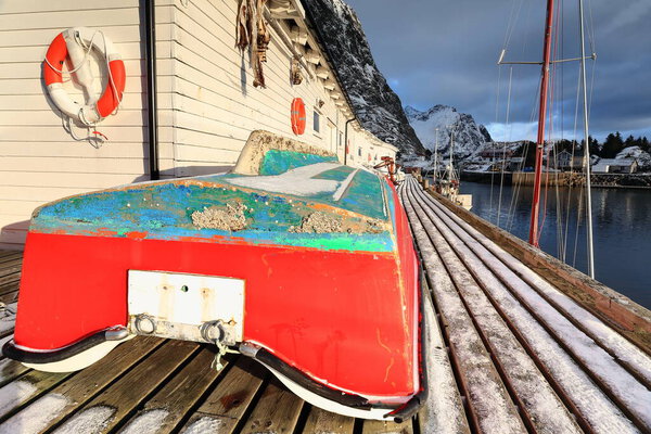 Small red-green fishing boats put ashore alongside white wooden warehouses on the pier deck-fishing port's W.side. Akkarviktinden mount background. Hamnoy-Reine-Moskenes-Lofoten-Nordland fylke-Norway