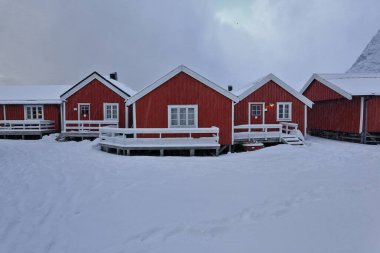 Festhaeltinden dağları üzerinde şiddetli kar yağışı ve turistlerin sudaki direkler üzerinde tek uçlu kullandıkları geleneksel balıkçı kulübeleri. Hamnoy-Reine-Moskenesoya-Lofoten-Nordland-Norveç.