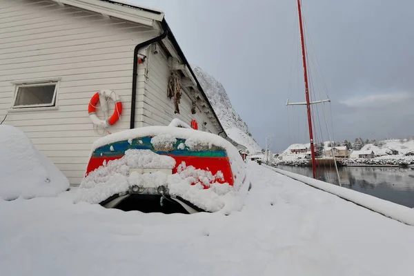 豪雪下の小さな赤緑の漁船が 漁港の西側にあるフェスタエルテンデン山の白い木製の倉庫桟橋デッキに沿って上陸します Hamnoy Reine Moskenes Looften Nordland Norway — ストック写真