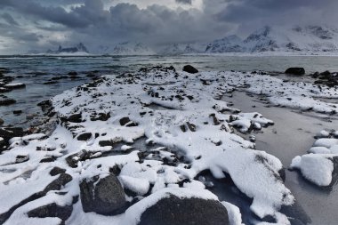 Neward manzaralı kar kaplı Ytresand plajı-Sandbotnen körfezi fırtınalı gökyüzü. Flakstadtinden-Digertinden-Storklauvan-Hustinden-Bjorntinden-Montinden-Hornet monları. Moskenesoya-Flakstadoya-Lofoten-Nordland-Norveç