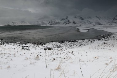 E-SEwards 'ın Ytresand' ı kaplayan kar manzaralı kumsal-Sandbotnen körfezi fırtınalı gökyüzü. Volandstinden-Sautinden-Nonstinden-Stortinden-Flakstadtinden tepeleri. Ytresand-Moskenesoya-Flakstadoya-Lofoten-Nordland-Norveç.