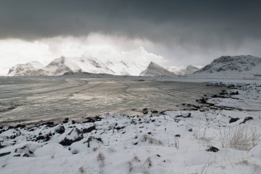 Deniz manzaralı kar, Ytresand plajı, Sandbotnen körfezi fırtınalı gökyüzü. Bora-Nesfjellet-Volandstinden-Sautinden-Nonstinden-Stortinden-Flakstadtinden atları. Moskenesoya-Flakstadoya-Lofoten-Nordland-Norveç