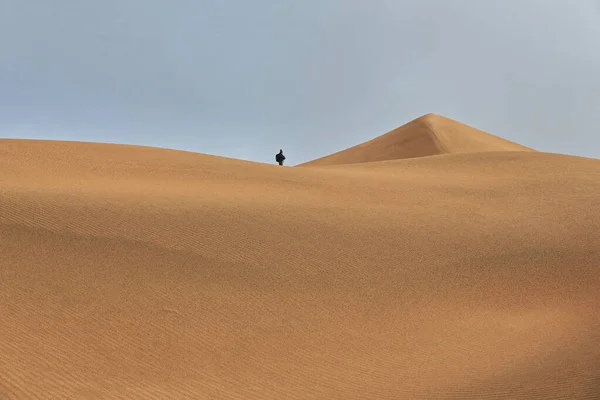 Tourist on a moving sand ridge viewing a pyramidal dune on the windward-W.facing slope of the megadune shaping Sumu Jaran and Sumu Barun Jaran lakes\' E.shore. Badain Jaran Desert-Inner Mongolia-China.