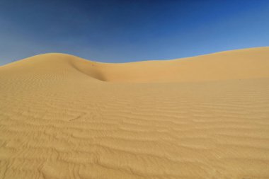 Wind-shaped hollow and pyramidal sand peak molded in the shifting sands topping the megadunes spread under the scorching sun and blue sky of the Badain Jaran Desert-Alxa Plateau-Inner Mongolia-China. clipart