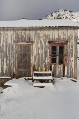 E10 Avrupa yolunun yanındaki Hustinden Dağı 'nın karla kaplı duvarına dayanan merdiven kenarındaki solmuş ahşap kulübeyi kar kapladı. Vareid-Flakstadoya-Lofoten-Nordland fylke-Norveç