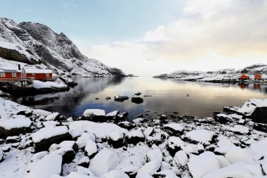 Kar, Vika bölgesinde Nusfjord balıkçı köyünün S.of 'una turist kullanımı için kırmızı ve ahşap balıkçı kulübeleriyle kaplı kıyı şeridini kapladı. Flakstadoya-Lofoten-Nordland Fylke-Norveç.