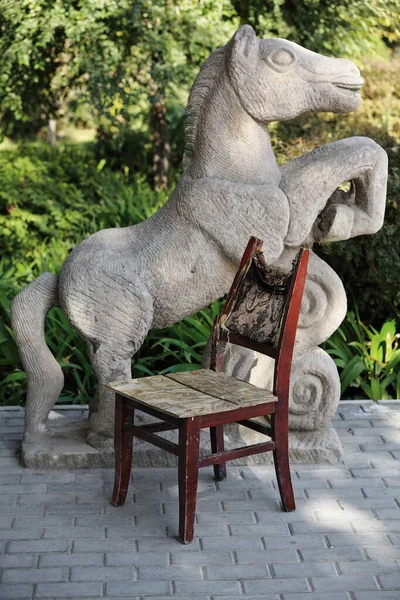 老旧的木制椅子 缺乏室内装饰的座位 背靠断了 在青翠的树阴下 在一匹骏马的雕像前安放着带铁丝的肩刃 甘泉公园 — 图库照片