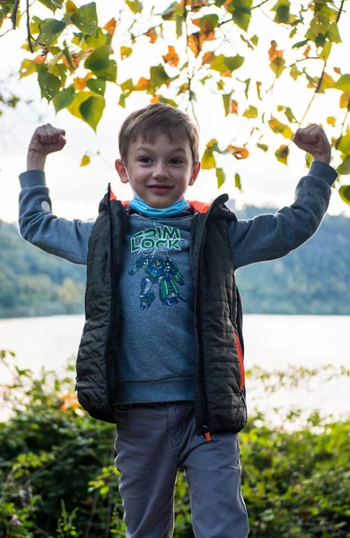 Niño sentado en un banco con una máscara médica. parque de otoño —  Fotos de Stock