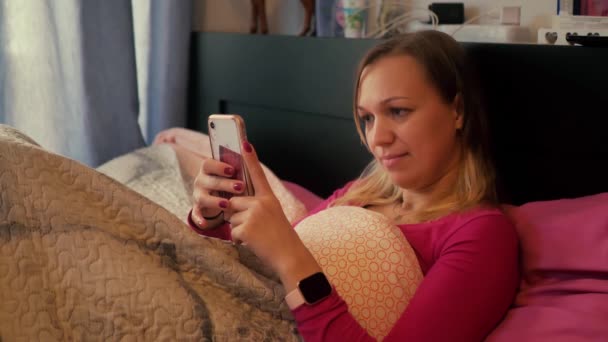 Frau im Bett schaut aufs Telefon — Stockvideo