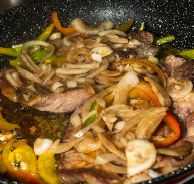 Biftek, soğan ve dolmalık biberle tatlandırılmış bir tavada pişirilir..