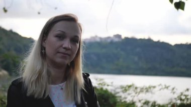 Parkta tek başına duran, gülümseyen ve kameraya bakan genç bir kadının yakın plan portresi. İnsanlar ve tarz kavramı