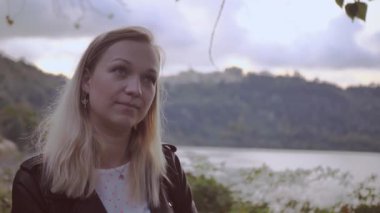 Parkta tek başına duran, gülümseyen ve kameraya bakan genç bir kadının yakın plan portresi. İnsanlar ve tarz kavramı