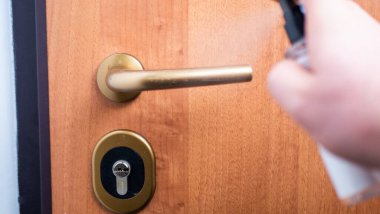 Bir şişe dezenfektan sıkarak kapı kolunu dezenfekte eden bir adamın yakın çekimi.