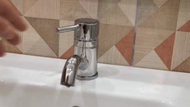 Banyoda musluk ve akan su. Su enerjisini korumak ve çevreyi korumak için insan sürekli olarak suyu kapatır.