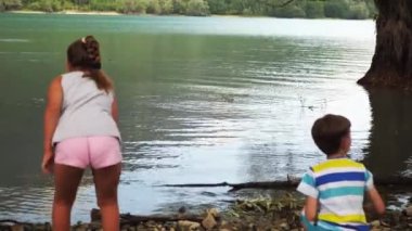 Oğlan ve kız suya taş atıyor.