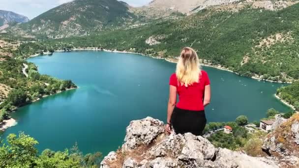 Weißhaariges Mädchen, das auf einem Felsen sitzt und die Berglandschaft aus einer Höhe betrachtet. See in Herzform — Stockvideo