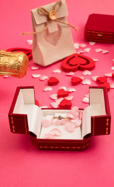 Vista superior sobre la mesa el día de San Valentín, 8 de marzo, Día de las Madres. con una botella de champán, una caja con un anillo, una caja de regalo con un lazo de cinta roja, corazones sobre un fondo rojo —  Fotos de Stock