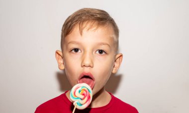 Bir çocuk çubuğun üzerinde çok renkli bir şeker yer. Elinde şeker lolipopu olan bir çocuk.