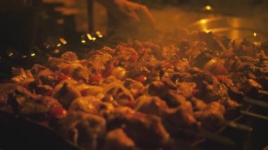 Yakın plan el, şişleri etle çevirir. Sıcak kömürde barbekü. Akşamları. Karanlık. Açık hava pikniği. Taştan yapılmış barbekü
