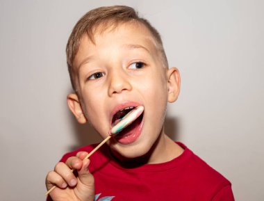 Bir çocuk çubuğun üzerinde çok renkli bir şeker yer. Elinde şeker lolipopu olan bir çocuk.