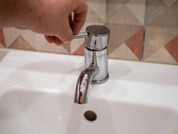 Adam banyodaki musluğu açıyor.