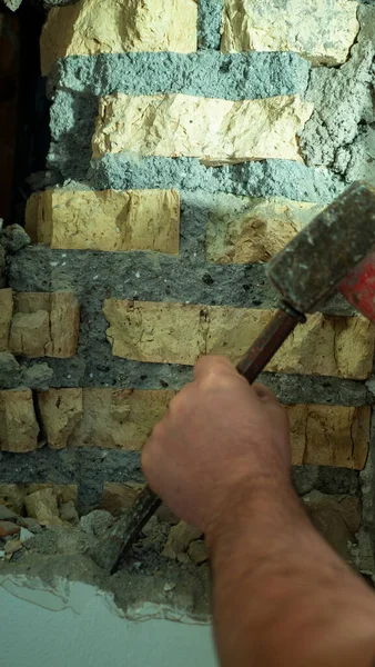 Byggaren slår ett hål i väggen med en hammare, närbild — Stockfoto