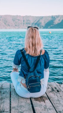 Sırt çantalı sarışın kadın sahile yakın tahta tahtalarda oturuyor..