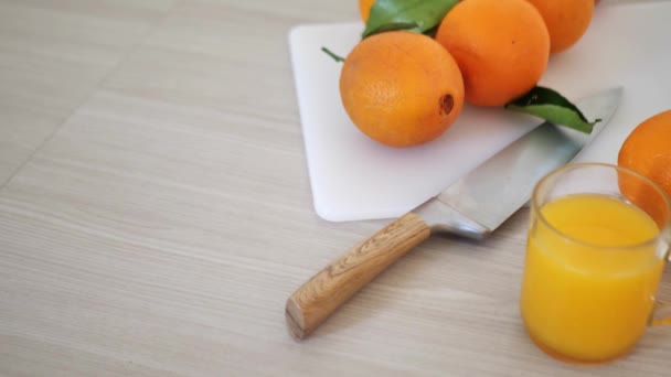 Свіжий апельсиновий сік у склянці, оточений апельсинами на сірому фоні — стокове відео
