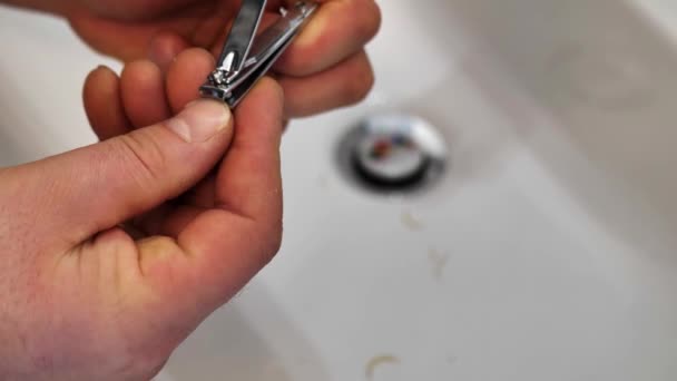 Człowiek rankiem tnie paznokieć nożyczkami nad umywalką lub umywalką. — Wideo stockowe