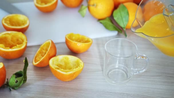 Наливаю свежий апельсиновый сок. Сжатые оранжевые детали на деревянной доске. Закройте стакан свежего апельсинового сока. Здоровое и вегетарианское питание. Фруктовые напитки на кухонном столе — стоковое видео