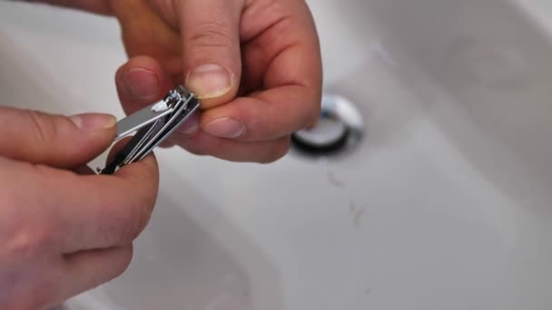 Молодой человек стрижет ногти над раковиной. — стоковое видео