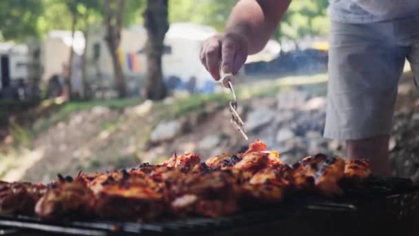 A male hand turns a delicious fried meat with a fork. Close-up of an unrecognizable man frying a delicious chicken on a barbecue outdoors. Leisure, cooking — Stock Video