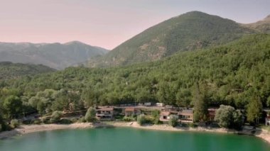 Turkuaz suyu ve yeşil ağaçları olan dağ gölü. Dağları, ormanı ve gölü olan güzel bir bahar manzarası. Hava görüntüsü. İnsansız hava aracı güzel bir dağ ormanı gölünün üzerinden geçti.