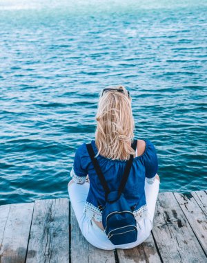 Sırt çantalı sarışın kadın sahile yakın tahta tahtalarda oturuyor..