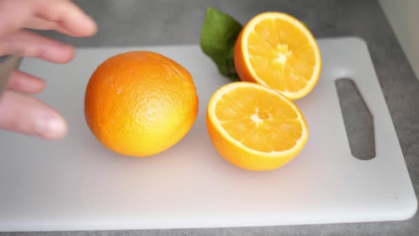 Mand hånd skærer en orange i halve med en kniv på et skærebræt – Stock-video