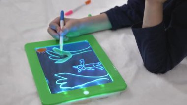 Bir çocuğun sanatsal çizimi, bir çocuk arka ışıklandırmalı tablet çiziyor.