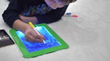 Çocuk çizim yapmak için telefondan hafif bir tablete geçiyor.