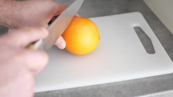 Zeitlupe Nahaufnahme männlicher Hände, die eine Orange mit einem großen Messer auf einem Schneidebrett halbieren. — Stockvideo