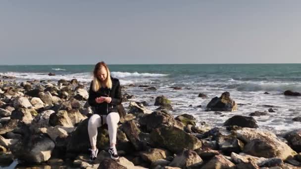 Mooi meisje zitten op een rots aan de zee en poseren voor de camera, het nemen van een selfie. — Stockvideo