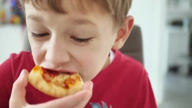 Pizza yiyen bir çocuğun yakın çekimi. Komik somurtkan bebek pizzadan ısırıyor