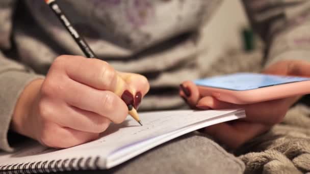 소녀 손은 집에서 스마트폰을 사용하여 숙제를 쓴다 — 비디오