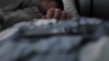 Genç adam sabahın erken saatlerinde mobil bir alarmdan uyanıyor. Kavram. Uykulu adam, akıllı telefonunda bir çalar saat duyduğunda uyanır ve bir cep telefonuna ulaşmaya çalışır.