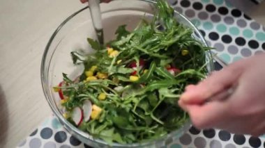 Bir kadının ellerinin cam fiyonkta vegan yeşil salata malzemelerini karıştırdığı izole edilmiş görüntüleri kapatın. Salatada roka, domates, marul, maydanoz ve tohum var..
