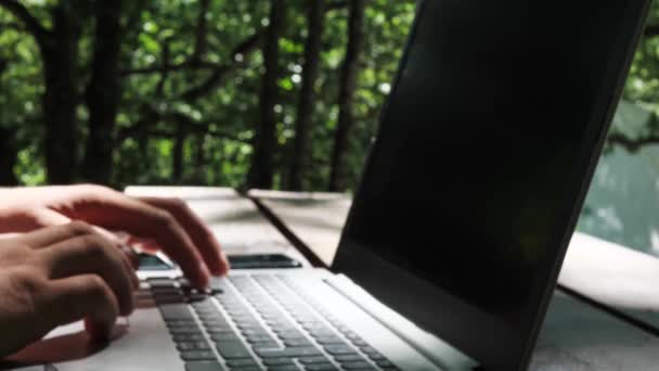 Человек работает на ноутбуке в природе, закрывает ноутбук. на заднем плане зеленые деревья — стоковое видео