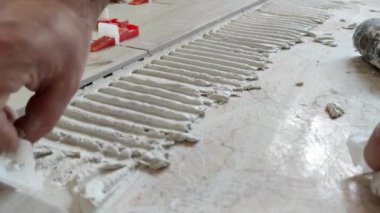 Bir işçi seramik fayansı takoz ve klipslerle düzleştiriyor. Döşeme seviyelendirme sistemi
