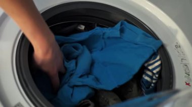 Kadın çamaşır makinesine çamaşır koyuyor.