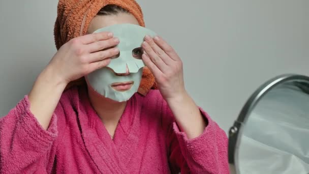 Mujer joven con una máscara en la cara se acuesta. Tratamientos de spa de belleza en casa para niñas. El concepto de cuidado de la piel, hidratación e hidratación. — Vídeos de Stock