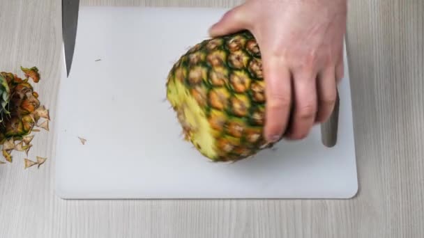 Geschlossen an den Händen eines Mannes, der eine Ananas auf einem Schneidebrett schneidet — Stockvideo