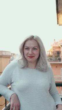 dikey video. Balkonda kırmızı dudaklı sarışın bir kadının portresi.